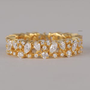 Puede incluir: Un anillo dorado con un patrón continuo de piedras preciosas claras de talla marquesa y redonda. La banda del anillo también es dorada, creando un diseño cohesivo y elegante. Las piedras están engastadas muy juntas.