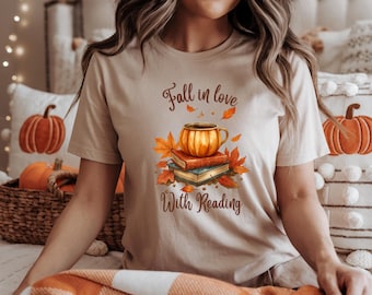 May include: A beige t-shirt with the text "Fall in love With Reading" and a graphic of a coffee cup, books, and autumn leaves. The shirt is made of a soft material and is perfect for fall.