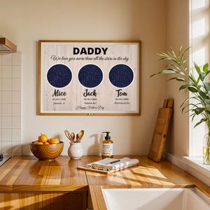 May include: Wooden framed print with the word "DADDY" and the text "We love you more than all the stars in the sky". The print features three dark blue star charts with names and dates below. The words "Happy Father's Day" are also included.