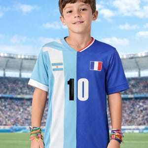 Puede incluir: Un niño lleva una camiseta de fútbol con un diseño dividido. Un lado presenta los colores y la bandera de Argentina, el otro lado los colores y la bandera de Francia. El número 10 está impreso en la parte delantera. También lleva pantalones cortos azules y pulseras coloridas.