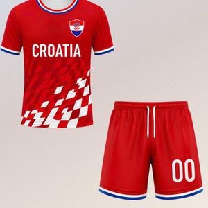以下が含まれることがあります： クロアチアの赤いサッカーユニフォームセット。ジャージには白い「CROATIA」の文字、クロアチアの紋章、白と赤のチェック柄があります。ショーツは赤色で、数字「00」が白で表示されています。