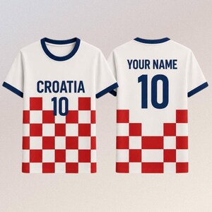 Puede incluir: Camiseta blanca con ribetes azul marino, con la palabra "CROACIA" y el n&uacute;mero "10" en azul marino. La parte inferior tiene un patr&oacute;n de cuadros rojos y blancos. La parte trasera muestra "YOUR NAME" encima del n&uacute;mero "10".