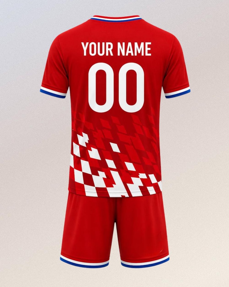 以下が含まれることがあります： 赤色のサッカーユニフォームとショーツのセット。ジャージには、白で「YOUR NAME」の文字と数字「00」が表示されています。ジャージとショーツには青と白のトリムが付いています。ジャージは赤と白のチェック柄です。