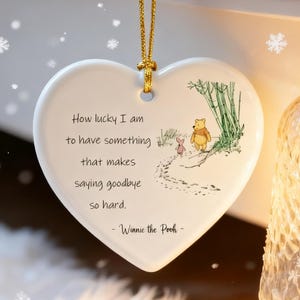 Puede incluir: Adorno de cerámica en forma de corazón con una cuerda dorada para colgar. El adorno presenta una ilustración de Winnie the Pooh y la cita: "How lucky I am to have something that makes saying goodbye so hard."