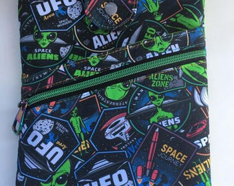 May include: A rectangular fabric pouch featuring a black background with a repeating pattern of green aliens, UFOs, and badges with text including UFO Area, Space Journey, and Aliens Zone. The pouch has a front zippered pocket and a snap closure.