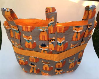May include: A quilted fabric tote bag featuring a repeating pattern of orange foxes on a gray background. The foxes are depicted wearing various accessories including glasses, hats, and neckties. The bag has orange trim and handles.