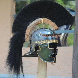 May include: A Roman helmet with a black plume. The helmet is dark green and gold with a curved visor and a decorative band around the base. The plume is long and flowing, adding to the helmet's imposing appearance.