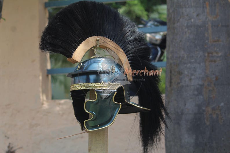 May include: A Roman helmet with a black plume. The helmet is primarily dark blue with gold trim and accents. The helmet is mounted on a wooden stand, showcasing its historical design and craftsmanship.