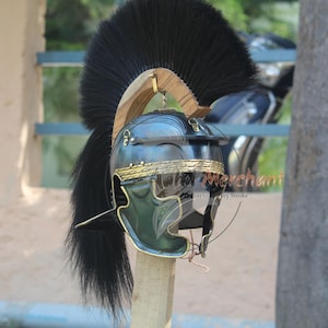 May include: A Roman helmet with a black plume, gold trim, and a dark green visor. The helmet is mounted on a wooden post. The helmet's design is reminiscent of ancient Roman military headgear.