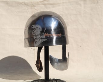 May include: A polished, silver-colored helmet with a rounded top and a face guard. The helmet has a leather strap and buckle. The helmet is displayed on a black stand. The helmet has a logo on the side.