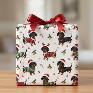 Puede incluir: Una caja de regalo envuelta con un lazo rojo. El papel de regalo presenta un patrón repetido de perros salchicha con gorros de Papá Noel y suéteres navideños. El fondo es blanco con pequeños iconos navideños.