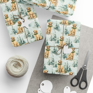 Puede incluir: Papel de regalo con un patrón repetido de golden retrievers con coronas, sobre un fondo de bosque nevado. Los regalos envueltos están atados con hilo y adornados con etiquetas en forma de corazón. También hay un carrete de hilo y unas tijeras.