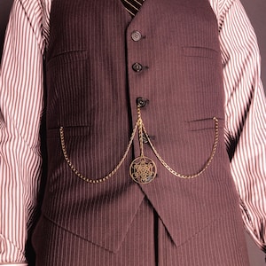 May include: A brown pinstripe waistcoat with a gold pocket watch chain and a decorative pendant. The waistcoat is buttoned and worn over a striped shirt and a striped tie. The waistcoat has two front pockets.