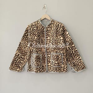Puede incluir: Una chaqueta acolchada con estampado de leopardo en marrón y negro, cuello redondo, mangas largas y dos bolsillos delanteros. Los bordes de la chaqueta, los bolsillos y los puños están ribeteados con tela a rayas blancas y negras.