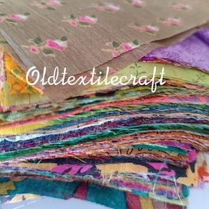 Puede incluir: Una pila de cuadrados de tela variados con diversos patrones y colores, incluyendo marrón con estampados florales rosas, morado, amarillo y verde azulado. El texto Oldtextilecraft está superpuesto en letras blancas sobre la tela superior.