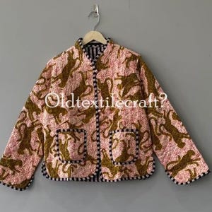 Pode incluir: Um casaco acolchoado com fundo rosa claro e um padrão repetitivo de animais em castanho escuro. O casaco tem uma gola mandarim, mangas compridas, dois bolsos frontais e acabamentos às riscas pretas e brancas nas bordas.