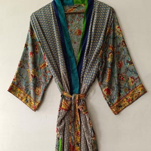 May include: A long-sleeved robe featuring a multi-patterned design with floral motifs in shades of gray, yellow, and red. The garment includes a solid teal and blue trim along the front opening and a matching fabric tie belt at the waist.