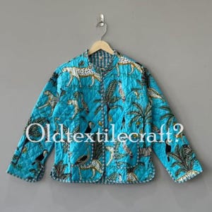 Könnte beinhalten: Eine gesteppte Jacke in hellem Türkis mit einem sich wiederholenden Muster aus Leoparden, Tukanen und Palmen in Schwarz, Weiß und Gelb. Die Jacke hat lange Ärmel, eine Knopfleiste und einen Kragen. Der Text Oldtextilecraft? ist sichtbar.