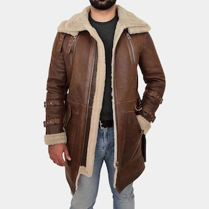 May include: A brown leather coat featuring a thick cream-colored shearling lining, a wide collar, and long sleeves with adjustable buckle straps at the cuffs and forearms. The coat includes vertical zippered pockets and a front zipper closure.