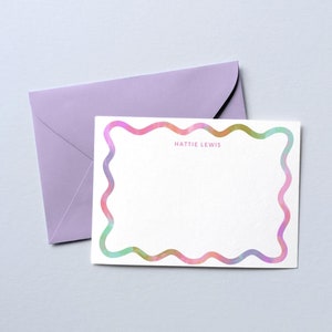 May include: A white card with a wavy, colorful border. The text "Hattie Lewis" is printed in the center of the card.