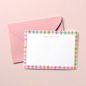 May include: A white card with a colorful plaid border and the name "PENNY HENDERSON" printed in black. The card is on top of a pink envelope.