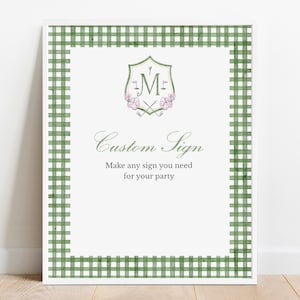 May include: A white sign with a green gingham border. The sign has a green and white crest with the letter "M" in the center. The text "Custom Sign" is written in cursive. Below the text is the phrase "Make any sign you need for your party."