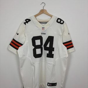 Op de afbeelding: Wit voetbalshirt met het nummer 84 in zwart op de voor- en achterkant. Het shirt heeft bruine en oranje strepen op de mouwen en het woord "BROWNS". Het Nike-logo is zichtbaar.