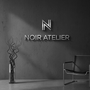 May include: A minimalist interior design scene featuring the text "NOIR ATELIER" in silver lettering on a dark gray wall. A modern chair and a glass vase with decorative branches are also visible.