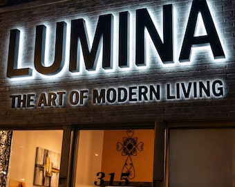 May include: Exterior shot of a storefront with the name "LUMINA" in large, illuminated black letters above the entrance. Below, the text reads "THE ART OF MODERN LIVING." The building is brick, and the shop windows display interior decor.
