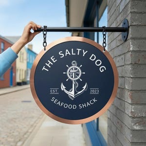 May include: A round sign for "The Salty Dog Seafood Shack" with a navy blue background and copper-colored trim. The sign features a white anchor and ship's wheel design, with the text "EST. 2023". The sign is hanging from a black metal rod.