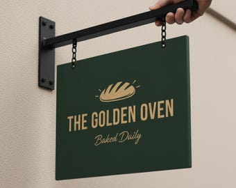 Peut inclure: Une enseigne vert foncé pour la boulangerie "The Golden Oven", soutenue par un support en métal noir. L'enseigne présente un texte doré et un dessin de pain, avec les mots "Baked Daily" en dessous. L'enseigne est suspendue à un mur beige.