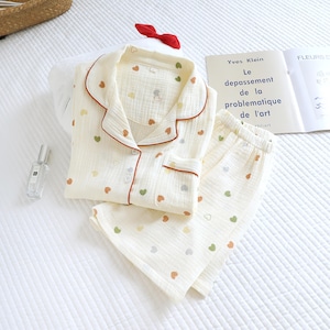 Puede incluir: Conjunto de pijama color crema con un estampado de corazones en varios colores. El conjunto incluye una camisa abotonada con ribete rojo y pantalones a juego. Tambi&eacute;n se ven un lazo rojo y un libro con el texto "Yves Klein".