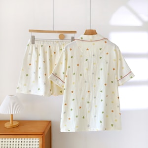 Puede incluir: Conjunto de pijama color crema con estampado de corazones. El conjunto incluye una camisa de manga corta con botones y pantalones cortos a juego. La camisa tiene ribetes rojos en el cuello y las mangas. Los pantalones cortos tienen cintura el&aacute;stica. Los corazones son verdes, amarillos y naranjas.