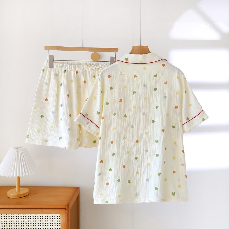 Puede incluir: Conjunto de pijama color crema con estampado de corazones. El conjunto incluye una camisa de manga corta con botones y pantalones cortos a juego. La camisa tiene ribetes rojos en el cuello y las mangas. Los pantalones cortos tienen cintura el&aacute;stica. Los corazones son verdes, amarillos y naranjas.