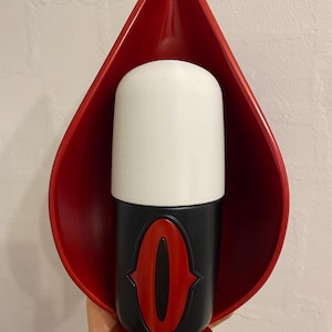 May include: A red, teardrop-shaped wall sconce with a white cylindrical light fixture and a black base featuring a red, stylized "0" emblem. The sconce is held in a hand against a neutral background.