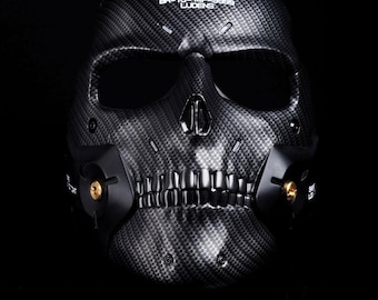 May include: A black skull mask with a carbon fibre weave pattern. The mask features eye sockets, a nose, and a jawline with teeth. The text "BR-10-14P-8888 LUDENS" is printed on the top.