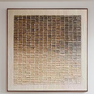 May include: A large square wall art piece featuring a grid of raised, textured rectangular blocks in a gradient of colors ranging from dark brown at the top to light cream at the bottom, framed in a thin, dark wood border on a white wall.