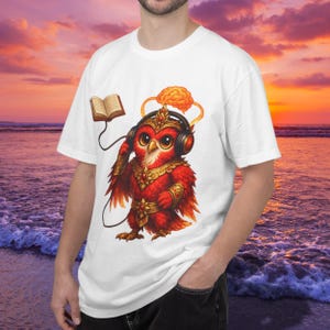 May include: White t-shirt featuring a cartoon owl wearing headphones and a crown, with a brain and book graphic. The owl is red with gold accents. The background shows a sunset over the ocean.