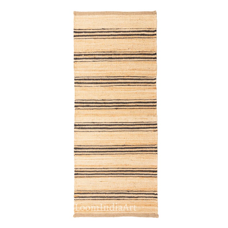 May include: A rectangular jute rug with horizontal black stripes. The rug has a natural beige color with dark brown stripes. The rug is made of woven jute material. The rug is suitable for indoor use.