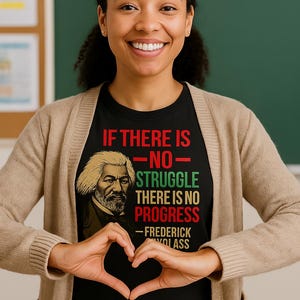 May include: Black t-shirt with a portrait of Frederick Douglass and the quote "If there is no struggle, there is no progress." The shirt is worn by a person wearing a beige cardigan. The background is a green chalkboard.