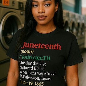 May include: A black t-shirt with the word "Juneteenth" in red, green, and yellow text. The shirt includes the definition of Juneteenth and the date June 19, 1865. The shirt is worn by a person with dark hair.