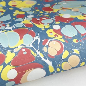 May include: A sheet of paper featuring a marbled pattern with a deep blue background. The design consists of organic, rounded shapes in shades of red, bright yellow, light blue, and cream, interconnected by thin, swirling white lines.