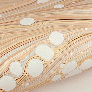 May include: A sheet of paper featuring a marbled pattern with swirling lines in shades of tan, beige, and light brown, interspersed with numerous solid white circular shapes of varying sizes that create a distinct contrast against the fluid background.