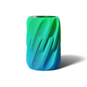May include: A cylindrical vase with a gradient of colors, transitioning from green at the top to blue at the bottom. The vase has a textured, ridged surface, creating a wave-like pattern. The vase is approximately 6 inches tall.
