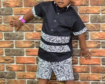 Puede incluir: Un niño viste un conjunto negro con detalles blancos, pantalones cortos a juego y zapatillas rojas. El conjunto se encuentra frente a una pared de ladrillos y césped verde.