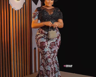 May include: A woman in a formal gown with a black bodice and a floral patterned skirt. The gown has a mermaid silhouette and a long train. She is wearing a matching head wrap and holding a small, beaded purse.