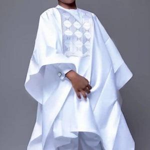 Könnte beinhalten: Ein weißes traditionelles Outfit für ein Kind, mit einer Tunika mit geometrischer Stickerei und passender Hose. Das Outfit beinhaltet eine kleine weiße Kappe und Sonnenbrille. Die Kleidung ist aus fließendem Stoff.