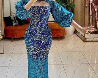 May include: A teal and navy blue patterned dress with a square neckline and long, puffy sleeves. The dress features a fitted bodice and a floor-length skirt. The fabric has a gold and navy blue leaf-like design. The dress is a formal wear item.