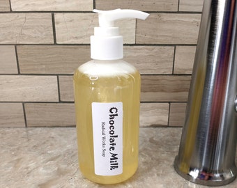 May include: A clear bottle of liquid soap with a white pump dispenser. The bottle has a label that says "Chocolate Milk" and "Radical Works Soap".