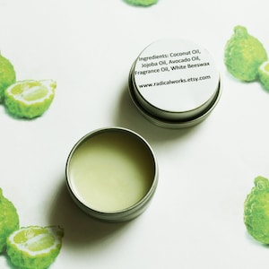 May include: Two small, open, silver tins of balm sit on a white surface, one with its lid beside it. The balm is light green. The lid has text that reads "Ingredients: Coconut Oil, Jojoba Oil, Avocado Oil, Fragrance Oil, White Beeswax, radicalworks.etsy.com". Green citrus fruit illustrations are scattered around the tins.